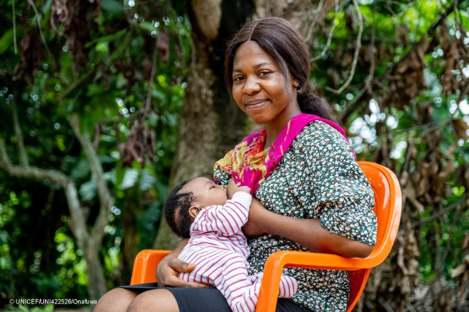 A woman breastfeeds her baby while sitting down on a chair.