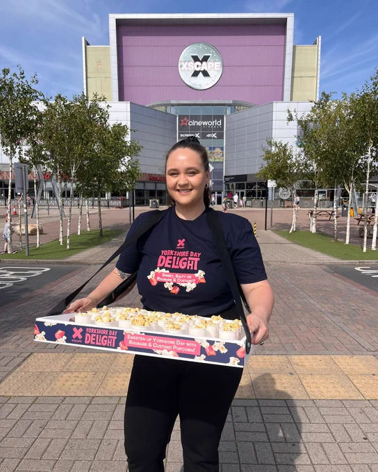 A person stands in front of the Xscape building holding a tray of popcorn with the text "Yorkshire Day Day Delight".