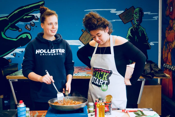 Photo of two young women who were participants in our Kitchen Kickstart programme. They are cooking together using a single hob.