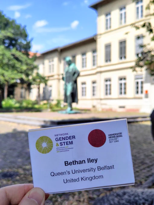 Name badge for the Network Gender and STEM 2024 Conference at Heidelberg University. It reads "Bethan Iley, Queen's University Belfast, United Kingdom". Behind the name badge is a university plaza with a statue in the centre.