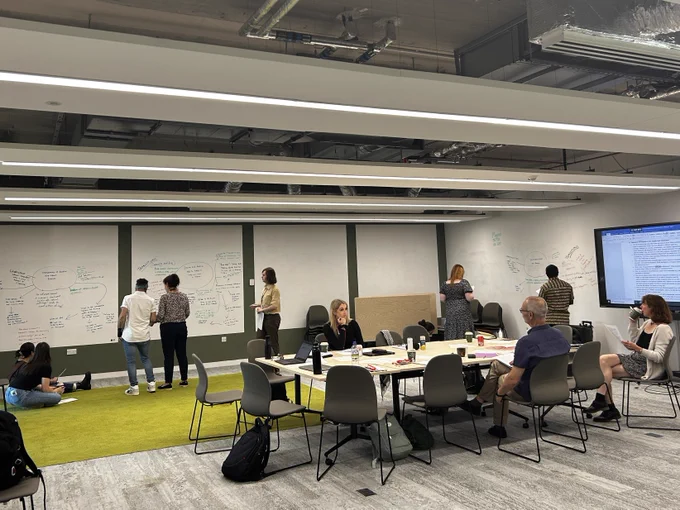 Group of people working on whiteboards while another group sit around a desk in conversation