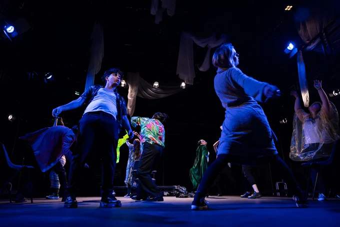 A group of actors in a dramatic dance performance on a stage with blue lighting, capturing energetic movement and expressive gestures.