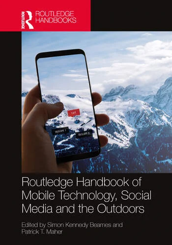 The cover of the 'Routledge Handbook of Mobile Technology, Social Media and the Outdoors'.  A background picture of a mountain, in the foreground there is a hand holding a mobile phone overlaying information about the mountain.