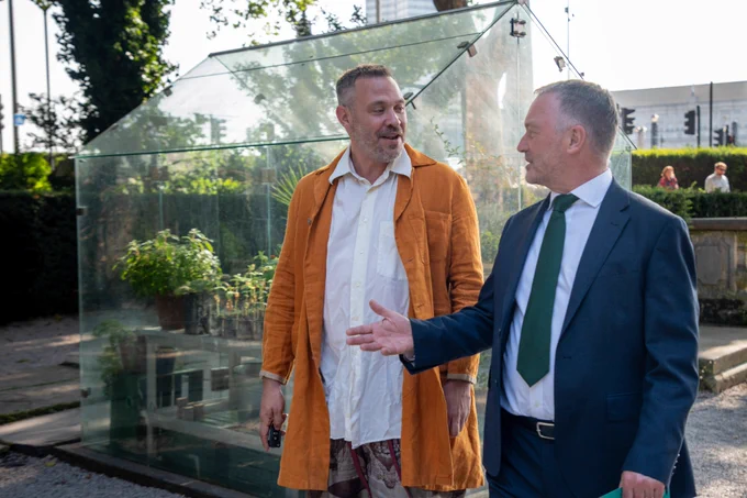 Secretary of state talking to singer, Will Young, by a greenhouse. 