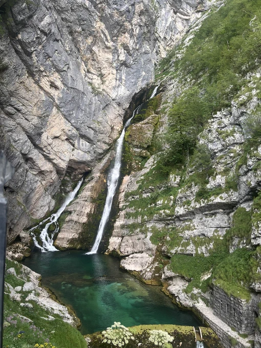 Photograph of a double waterfall coming down a mountain. The pool at the bottom is crystal clear.