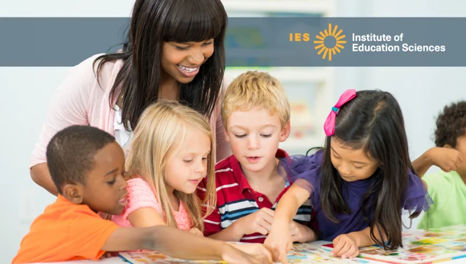 A kindergarten teacher standing behind a group of students as they look at a map together. Behind the teacher is a gray overlay with the Institute of Education Sciences logo.