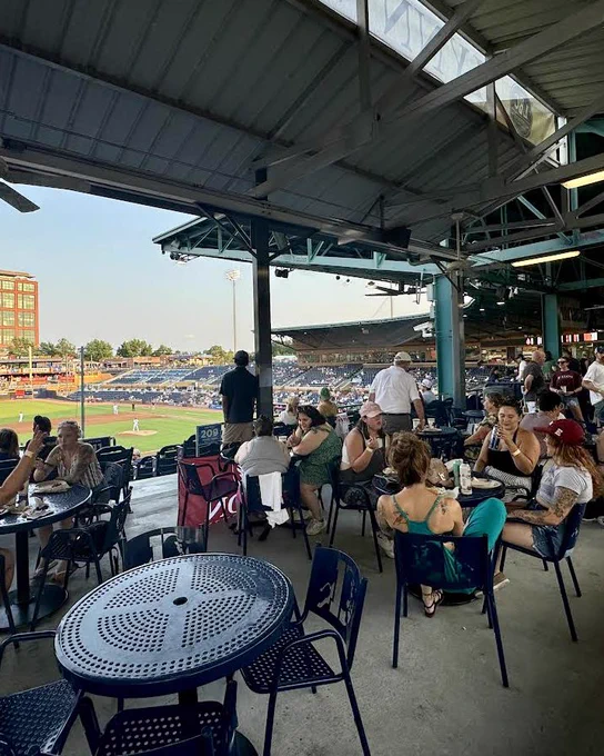 Group of Elon alums socializing at tables on a terrace at Bulls baseball game
