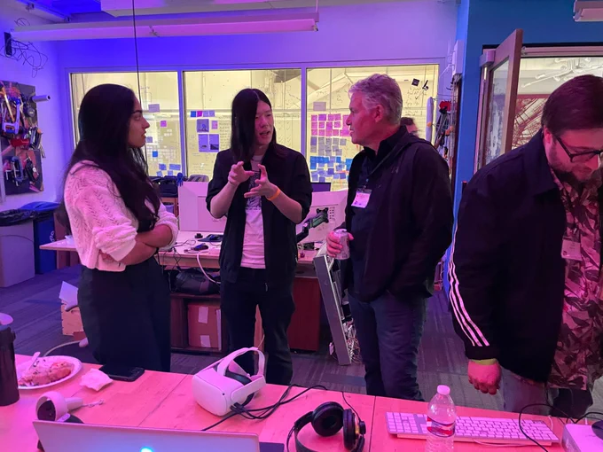 Three attendees of a conference in a discussion about research. Foreground is a VR headset and headphones on a table.