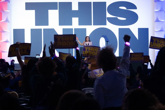 Vice President Kamala Harris speaking to a crowd. The crowd is holding signs and the stage reads, "This Union" in blue letters. 