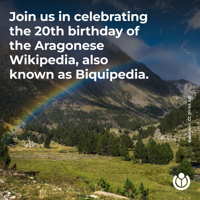 A colorful rainbow spans a green valley dotted with trees, set against a backdrop of mountains and a partly cloudy sky. Text says “Join us in celebrating the 20th birthday of the Aragonese Wikipedia, also known as Biquipedia.”