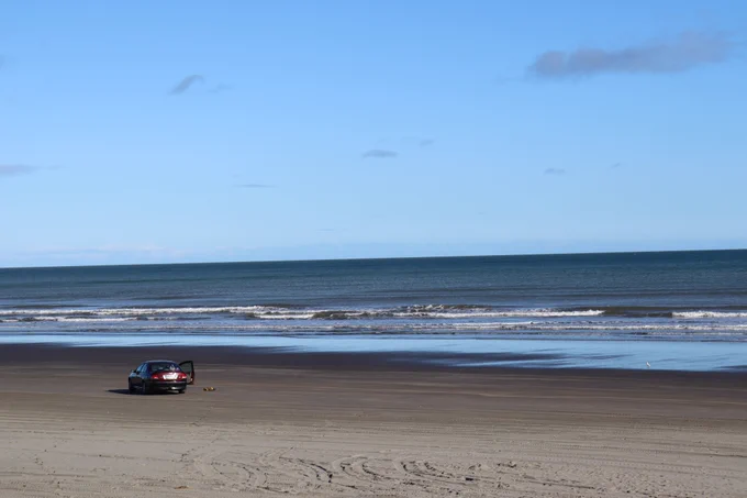 A lone car parked on the flat beach near the water. 