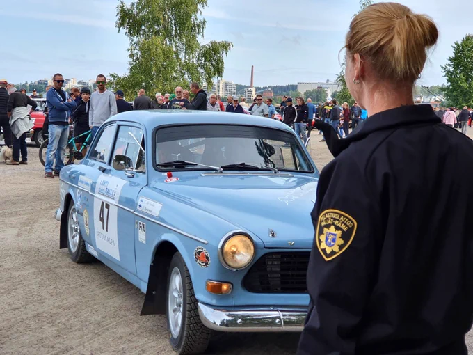 Siniseen pelastusalan virka-asuun pukeutunut nainen yleisötapahtumassa. Taustalla vanha auto.