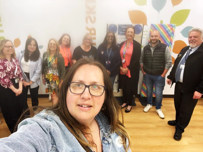 A selfie taken by Jenny, in the foreground, with nine volunteer managers behind her. Everyone is smiling for the camera!