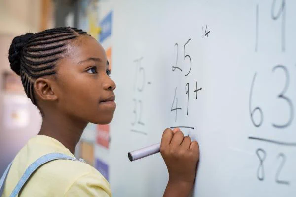 A girl solves math problems on a whiteboard.