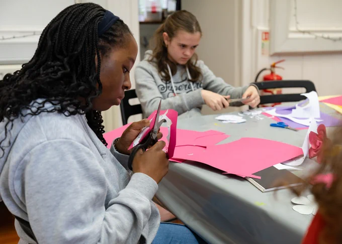 Two young people wearing grey hoodies concentrate on cutting flowers from pink and white paper