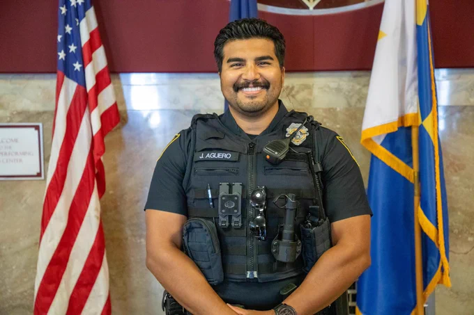 Officer Aguero smiles between the American Flag and Topeka Flag.