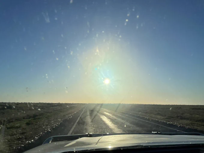 Photo through the windscreen of a Ute showing the morning sun, a lot of glare, and a very flat horizon.