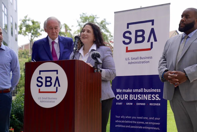 Administrator Guzman speaks at a podium with the SBA logo and signage. Senator Markey and three others are in the background