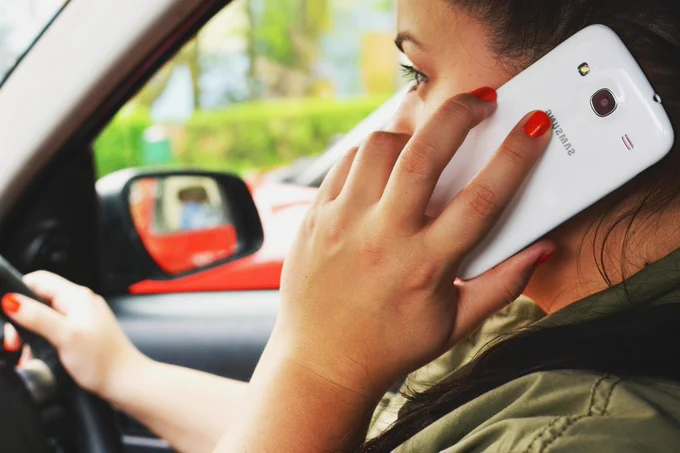A person driving a car whilst holding a mobile phone to their ear.