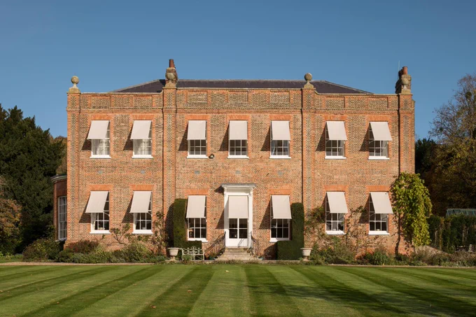 A photograph of a 2-storey, symmetrical country house with awnings over the windows.