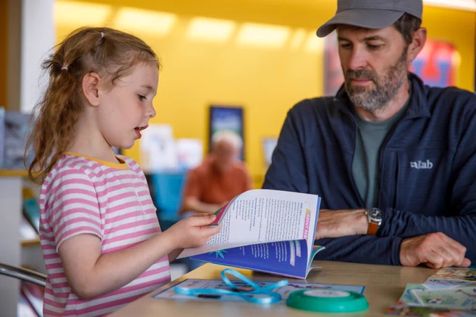 A girl is talking about the book she is holding to her father.