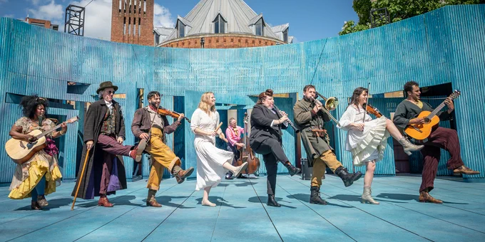 The company of As You Like It stood in a line holding instruments and dancing with their right leg raised