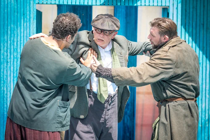 Three men stood in a huddle with their hands on each others shoulders looking concerned 