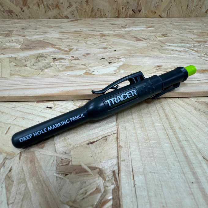 A black deep hole marking pencil with a green tip and a pocket clip, labeled "TRACER" on its side, lying on a wooden surface.