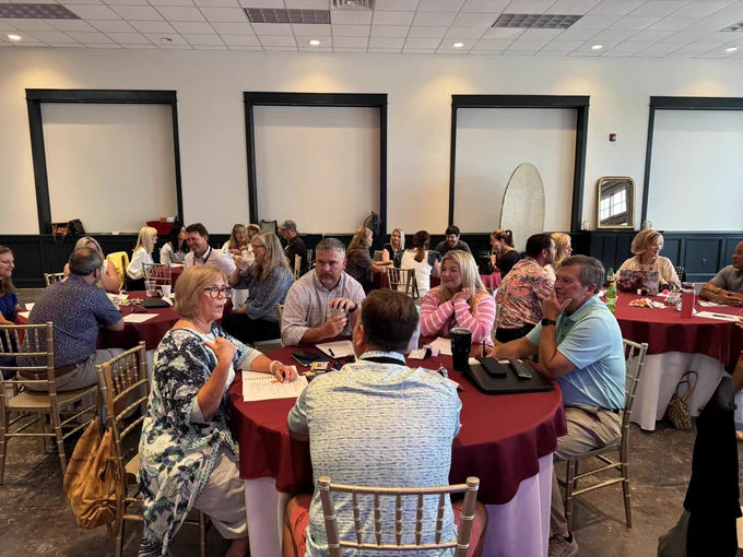 Group of school system leaders sitting around tables, talking to one another.