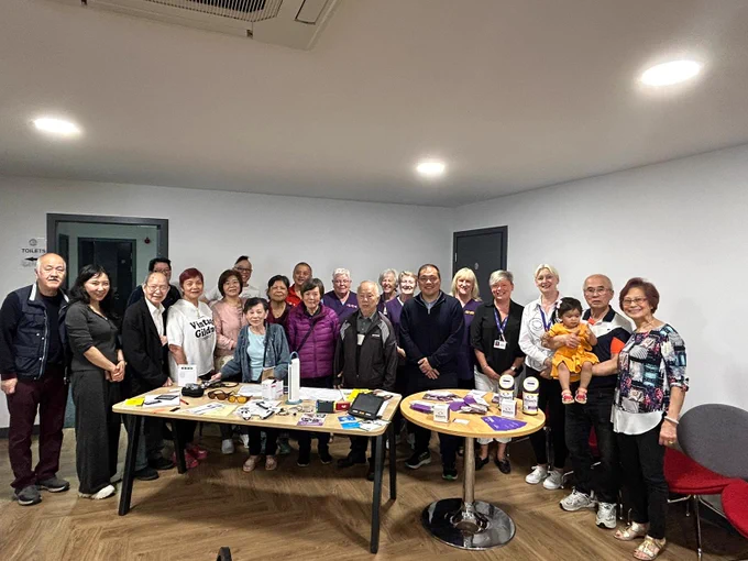 A large group of  members from the Perth Chinese Community Association, men, women and children standing behind a desk smiling.