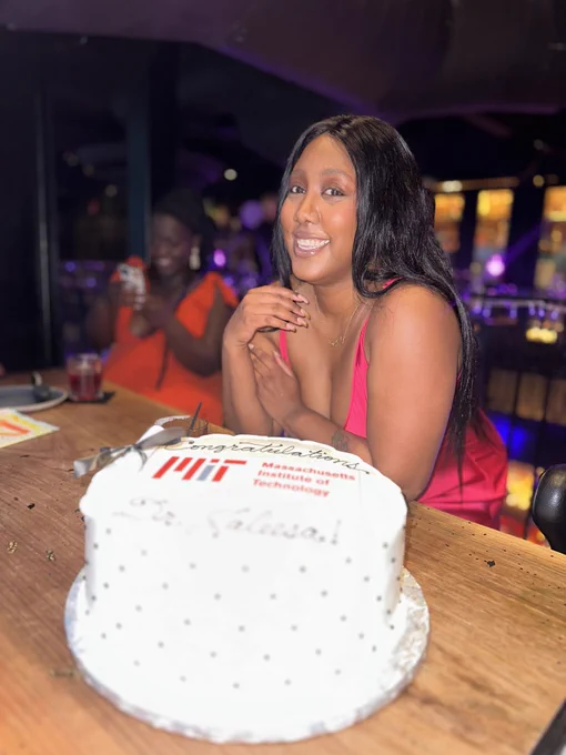 I'm smiling, wearing a pink dress. I'm wearing my hair straightened. I'm posing behind a graduation cake. The cake says congratulations, and has the MIT logo underneath.