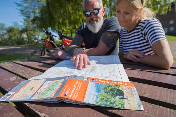 Two people sat at a picnic table, looking at an Ordinance Survey Explorer map of the National Forest.  Credit: National Forest Company