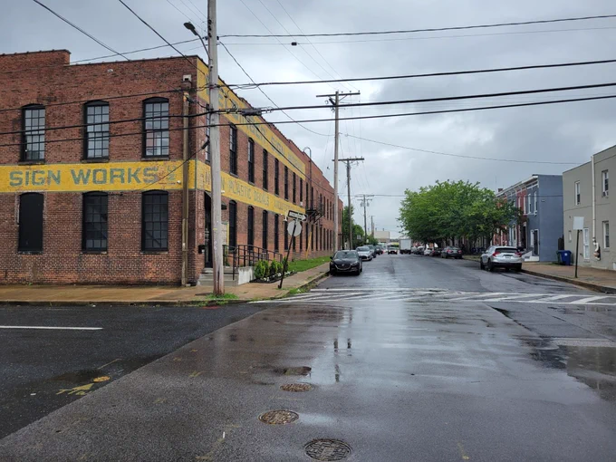 Brown warehouse with yellow banner near rainy street and grey sky.