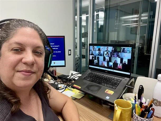 Amie Pilgrim takes a photo wearing headphones and documenting a Zoom call with participants.