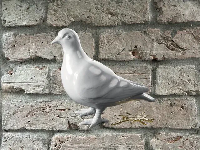 A ceramic pigeon sculpture mounted on a brick wall.