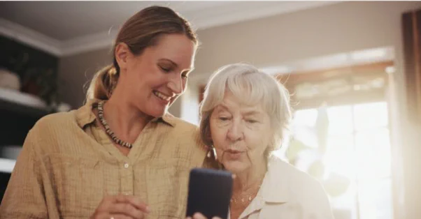 2 women standing together smiling and looking at a mobile phone screen