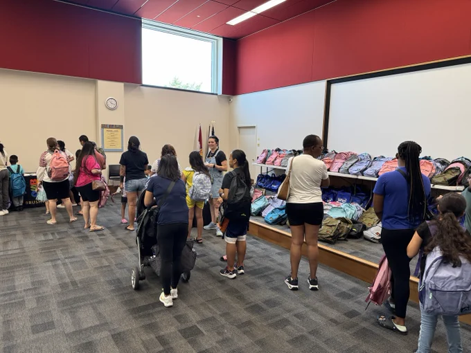 Photo of a line of children and adults waiting to get a free backpack full of school supplies at the library's back to school event. 