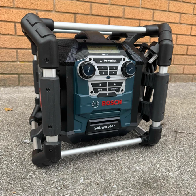 A Bosch PowerBox radio and subwoofer system placed on a brick pavement, surrounded by a black protective roll cage.