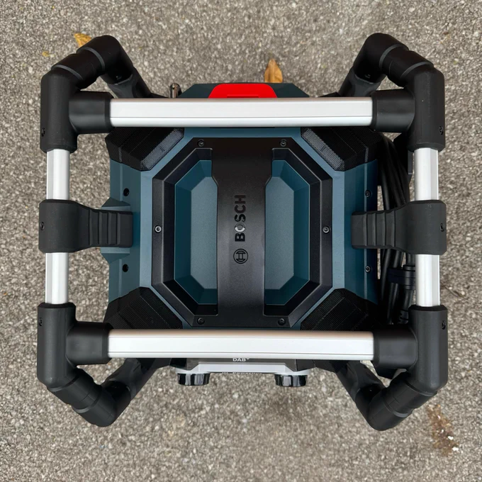 Top-down view of aBosch radio showing its distinctive black and blue body structure and roll cage, set on a concrete surface with fallen leaves around.
