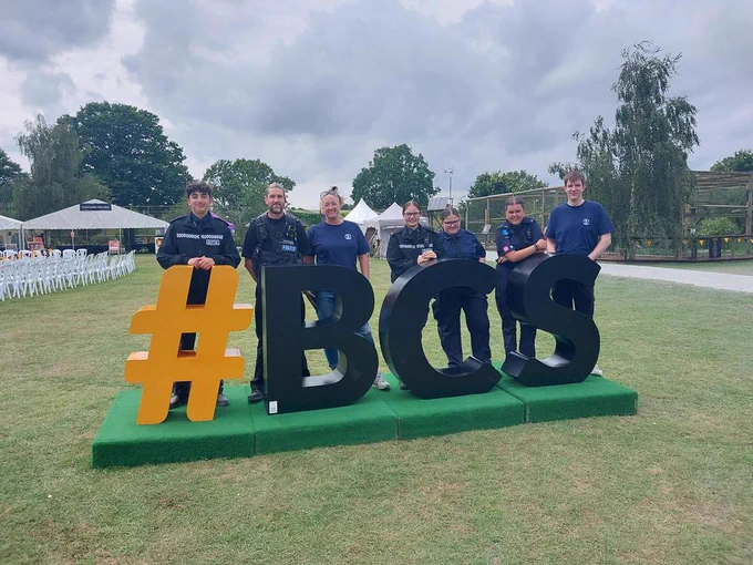 Cadets leaders and cadets at Big Cat Sanctuary stood behind a large #BCS sign on a field

