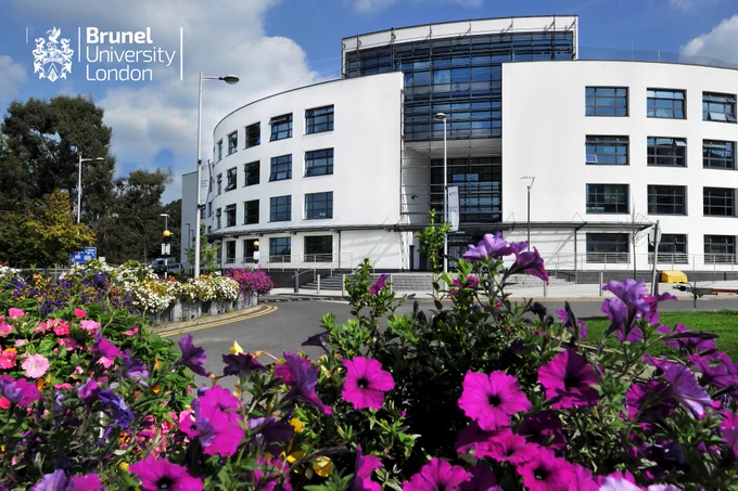 Blue sky and clouds with a tall circular building with a road leading to a row of flowers