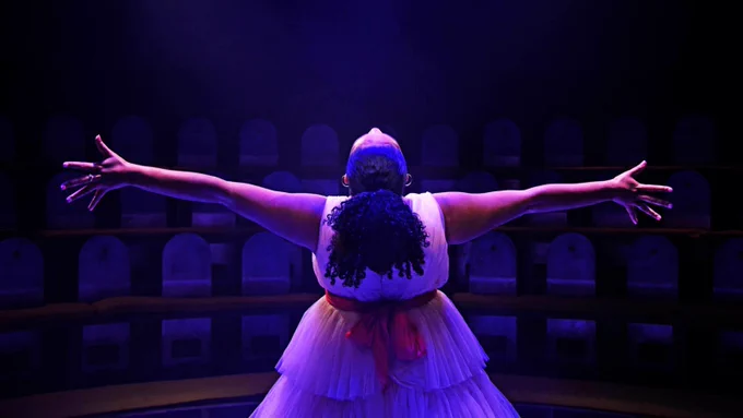 Photograph of a performer with their arms spread under blue and purple light