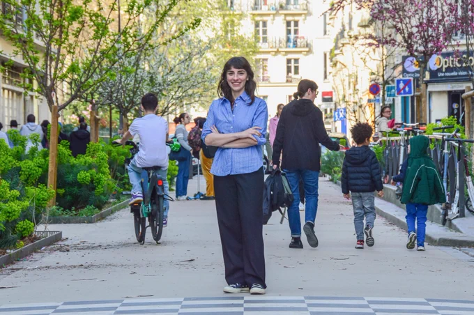 A car-free “school street” in Paris filled with playing children includes bike parking, vegetated areas, blossoming trees, and white asphalt painted with colourful games.