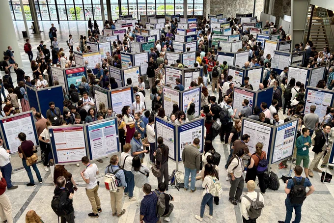 A large conference hall filled with numerous attendees engaging in a poster session.