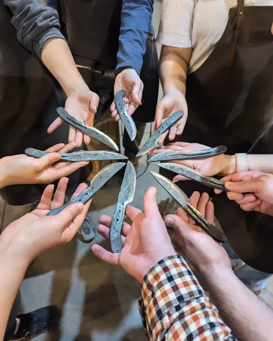 9 hands hold out their individually hand forged knives
