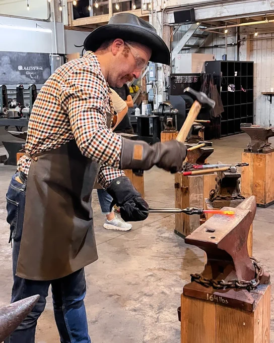 Joe hammers a piece of molten iron over an anvil