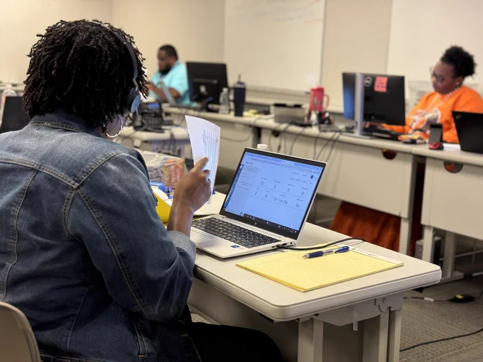 An adult sits at a table with a computer.
