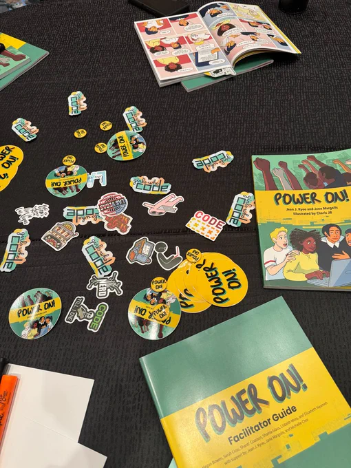 This picture shows copies of the Power On! graphic novel created by former CSTA Equity Fellows, as well as branded stickers. The book's colors are teal and yellow. This novel was used to guide and inform the workshop.