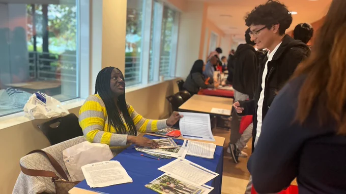 A student smiles while talking to a college admissions representative sitting at a table.