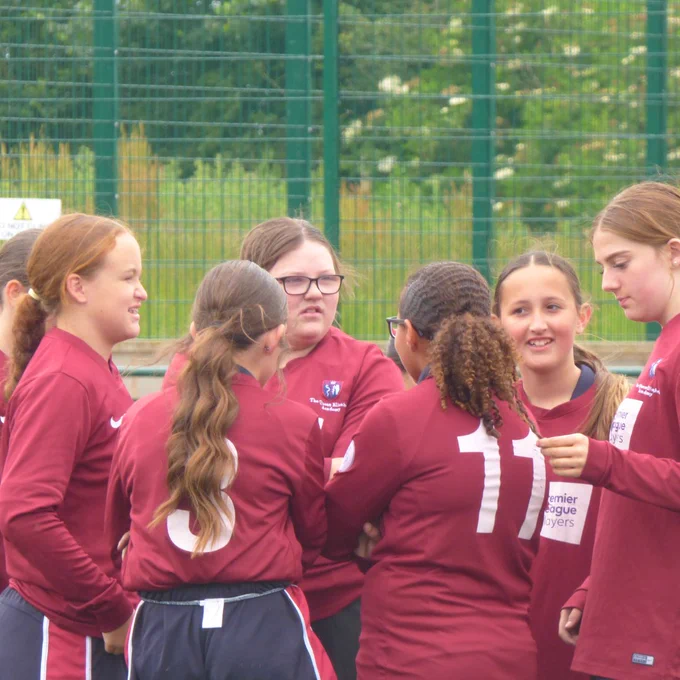 [Image shows a group of girls in football kits discussing the game they just played]